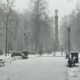 Первый снег в городском парке с пустыми скамейками и памятной колонной